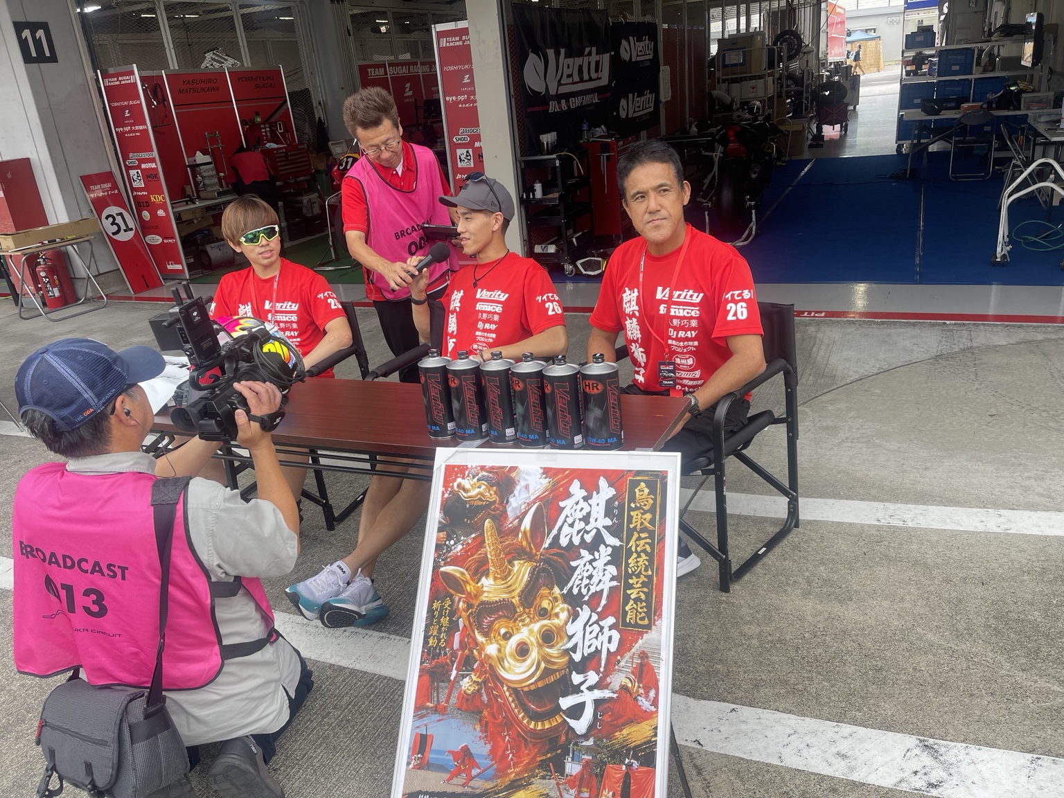 ピット前で取材を受けるチームと麒麟獅子の掲示